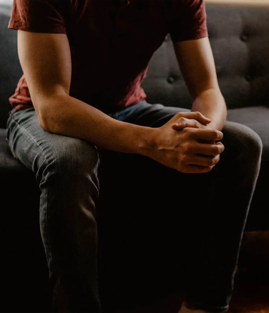 A person leaning with their elbows on their knees and their hands folded